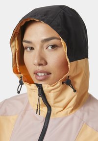 Chaqueta con capucha en melocotón y negro, hecha de un tejido ligero. Cuenta con cierre de cremallera, cordones ajustables y colores contrastantes.