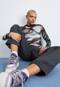 Fitted black mesh long-sleeve top with abstract iridescent patterns; gray loose-fitting pants; pastel purple and navy sneakers with stripes.