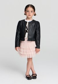 Giacca nera in ecopelle con zip frontale, orlo a coste e maniche a sbuffo, abbinata a una gonna in tulle rosa a strati e scarpe nere.