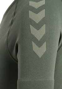 Olivgrön sweatshirt med ribbad textur och en tight design. Anmärkningsbart ljusgrönt chevronmönster tryckt på den övre ärmen.