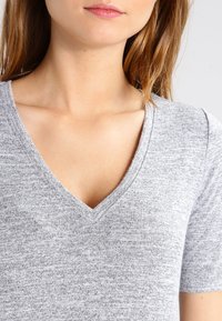 T-shirt grigio a scollo a V realizzato in morbido tessuto a maglia. Caratterizzato da maniche corte e una vestibilità comoda. Testura sottile con un motivo mélange.