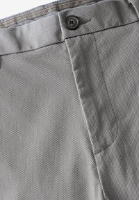 Tissu gris texturé avec fermeture à bouton, présentant des coutures visibles et un motif subtil. Le design inclut un détail de poche incurvée.
