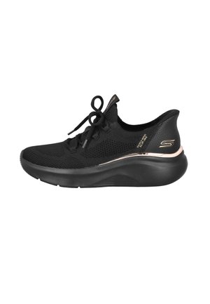 Zapatilla deportiva negra con parte superior de tela de punto, cordones, silueta elegante, talón texturizado y una franja metálica decorativa. Suela de goma suave.
