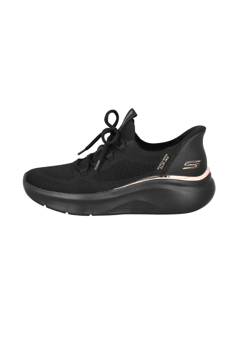 Zapatilla deportiva negra con parte superior de tela de punto, cordones, silueta elegante, talón texturizado y una franja metálica decorativa. Suela de goma suave.