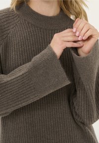 Grå, ribbad stickad tröja med hög, rund halsringning och breda, utsvängda ärmar, som visar upp en mjuk textur och avslappnad passform.