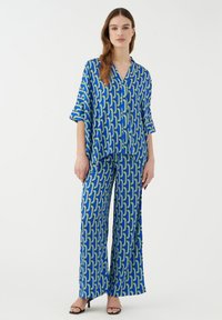 Conjunto de patrón geométrico en azul y verde que incluye una camisa holgada de manga corta y pantalones de pierna ancha. Textura de tela suave.