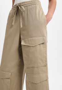 Beige cargobroeken met een elastische tailleband, voorzien van twee grote zijzakken en een relaxte pasvorm, gemaakt van een lichtgewicht stof.