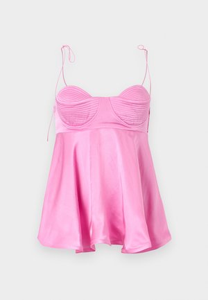 Femme portant un haut sans manches rose brillant avec de fines bretelles et une jupe midi blanche fluide, talons noirs à brides, posant avec une main sur la hanche.