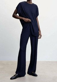 Pantalons larges texturés en marine et haut ample, fabriqués en tissu léger, associés à des mocassins noirs. Design simple et moderne.