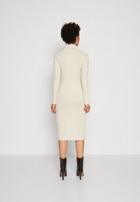 Robe midi beige à côtes avec manches longues et col, présentant une silhouette ajustée. Portée avec des bottines noires.