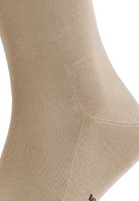 Calzino beige alla caviglia con una texture a maglia fine e liscia e punta rinforzata. Presenta un branding minimale sul tallone. Materiale morbido ed elastico.