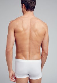 Vita bomullsboxer kalsonger som bärs av en man, som visar en bar rygg och axlar. Slät textur, åtsittande design och enkel midjeresår.