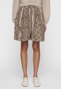 Pantalones cortos con patrón de serpiente en marrón y crema, con cintura elástica, dos bolsillos laterales y un ajuste holgado. Combinados con zapatos de color claro.