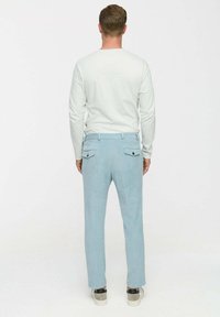 Hellblaue Cordhosen mit geradem Schnitt, ausgestattet mit zwei Gesäßtaschen und einer dezenten, gerippten Textur. Getragen mit einem weißen Langarmhemd.