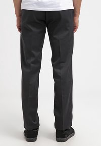 Pantalon noir à coupe droite, en tissu lisse. Comprend deux poches arrière et est assorti à des chaussures noires.