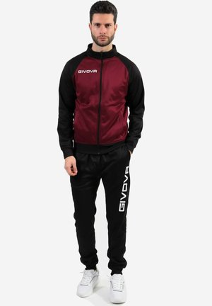 Giacca sportiva maroon e nera con zip e colletto alto, abbinata a pantaloni neri con logo bianco "GIVOVA". Sneakers bianche completano il look.