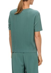 Turkusowa bluzka z prążkowanego materiału, z krótkimi rękawami i luźnym krojem, z okrągłym dekoltem i gładką fakturą. Pokazana z pasującymi spodniami.