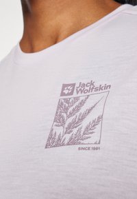 Tricou alb din bumbac, cu un design subtil imprimat în violet ce reprezintă frunze și cu logo-ul "Jack Wolfskin" plasat în partea stângă sus.