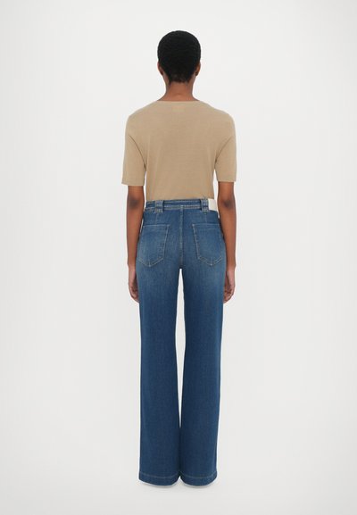 Brun kortermet topp kombinert med høytlivs, vid bukse i mørk blå denim, med baklommer og et rent, uopprørt design.