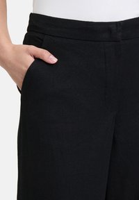 Zwarte linnen pantalon met een gladde textuur, voorzien van een voorzak en een platte tailleband voor een gestroomlijnd ontwerp.