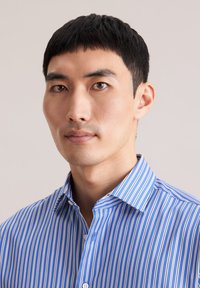 Niebiesko-biała koszula w paski z kołnierzykiem, zapinana na guziki z przodu, wykonana z gładkiego materiału, noszona przez osobę o krótkich ciemnych włosach.