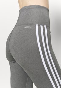 Leggings grigi alti in vita con dettagli a strisce bianche. Realizzati in un tessuto elastico, con il marchio "AEROREADY" sul retro.