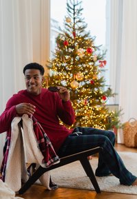 Comfortabele houten stoel met een donkere afwerking, een zacht geruit deken, een rood shirt met lange mouwen en groene geruite broek, in een warm verlichte feestelijke omgeving.