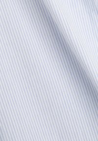 Tissu blanc avec de fines rayures bleues verticales légèrement plié, montrant les détails de la texture et du motif.