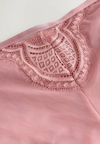 Világos rózsaszín fehérnemű, finom csipke díszítéssel a deréknál, sima, puha szövet textúrával és diszkrét fényességgel.