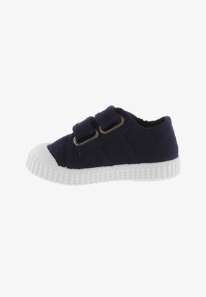Zapatillas infantiles de lona en color navy con dos correas ajustables, puntera de goma blanca y suela blanca texturada. Diseño estándar de corte bajo.