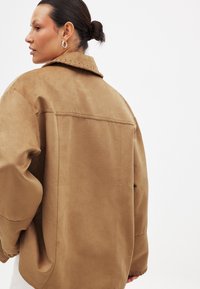 Pruun nahast jakk suurte kraedega, allalangetatud õlgadega ja mugava lõikega. Omab dekoratiivset tikandit krae ja õmbluste ääres.