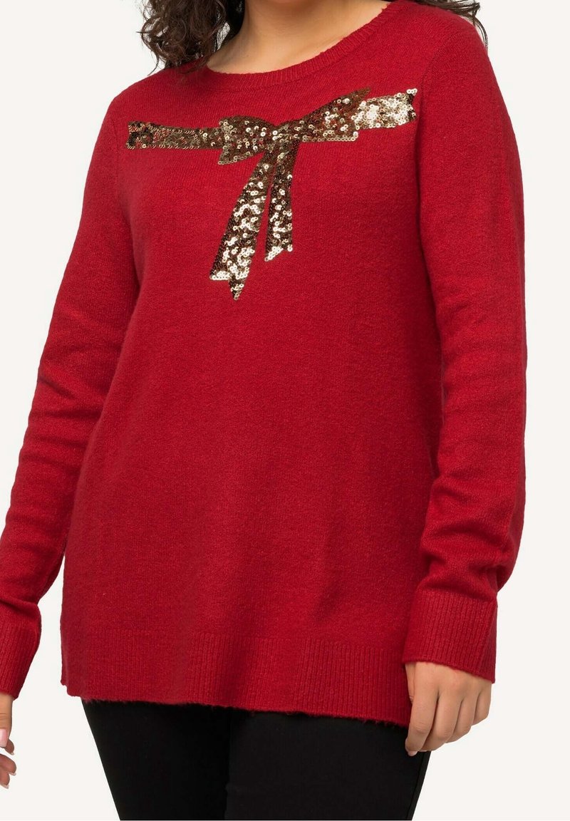 Czerwony sweter z miękkiego materiału z okrągłym dekoltem, ozdobiony kokardą z cekinów na piersi oraz ściągaczami przy mankietach i u dołu.