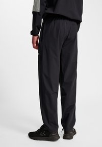 Zwarte, lichtgewicht sportbroek met een elastische tailleband, zijzakken en een gladde textuur. Gecombineerd met zwarte sportieve schoenen met een gestructureerd ontwerp.