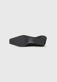 Zapato de tacón alto de ante negro con puntera afilada y suela plana texturizada con un leve tacón. Diseño limpio con acentos mínimos.