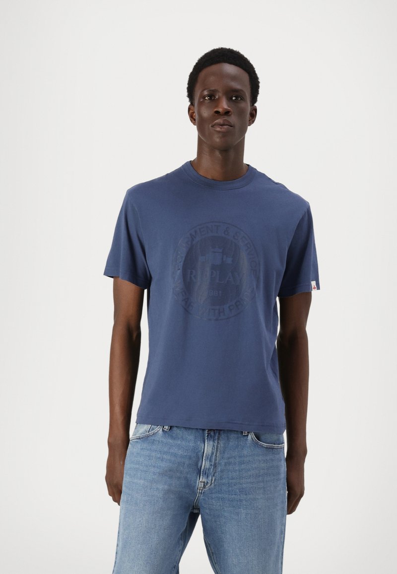 Camiseta de color azul marino hecha de algodón, con cuello redondo y mangas cortas, con un diseño de logotipo circular en el centro.