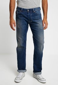 Mörkblå denimjeans med rak bendesign, ljus blekning, sydda fickdetaljer och standard knäppning, bärs med vita sneakers.