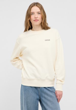 Kremowy sweatshirt z prążkowanymi mankietami i dołem, z delikatnym logo "Mustang" w kontrastowej czcionce na piersi. Miękka struktura materiału.