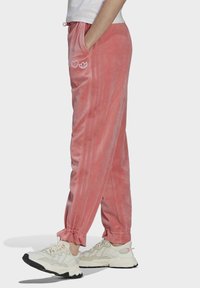 Rosa velour-joggingbyxor med sidofickor, elastiska mudd och dragsko i midjan. Accenteras av vita broderade logotyper på framsidan.