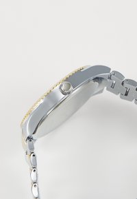 Montre en acier inoxydable argenté avec une lunette accentuée d'or, un boîtier rond et un bracelet à maillons. Dotée d'une couronne à bouton-poussoir et d'une finition lisse.