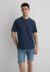 Navy blue short-sleeve t-shirt with white horizontal stripes, crew neck, paired with denim shorts. Cotton fabric with a smooth texture.
