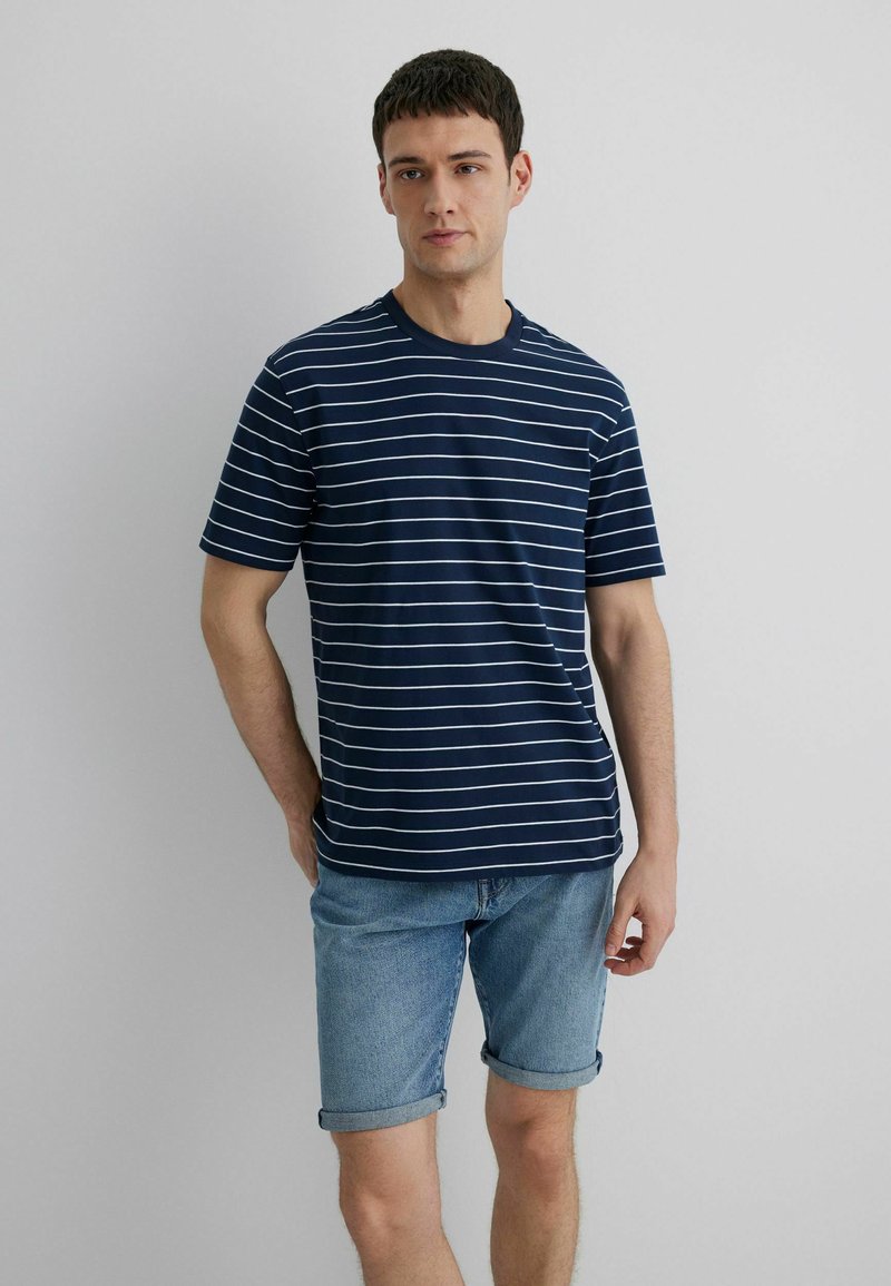 Navy blue short-sleeve t-shirt with white horizontal stripes, crew neck, paired with denim shorts. Cotton fabric with a smooth texture.