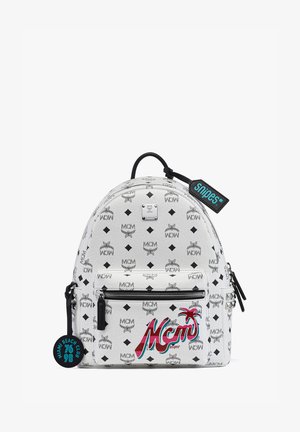 Sac à dos blanc avec motif logo MCM, forme arrondie, poche zippée à l'avant et accents noirs. Inclut une étiquette décorative portant l'inscription "Snipes".