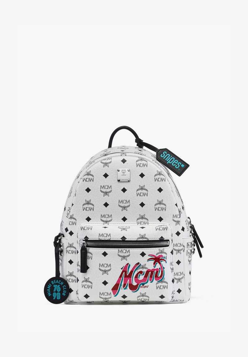 Weißer Rucksack mit MCM-Logo-Muster, runde Form, vorderes Reißverschlussfach und schwarzen Akzenten. Enthält ein dekoratives Etikett mit der Aufschrift "Snipes."