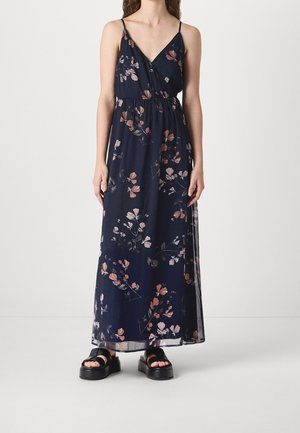 Woman wearing a navy blue floral sleeveless maxi dress with spaghetti straps and black platform sandals, standing against a plain background.