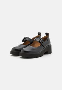 Black leather shoes with a round toe, adjustable buckle, and a chunky platform heel. Interior features brown lining and minimal stitching details.