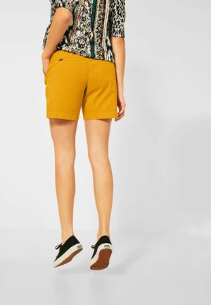 Yellow cotton shorts with a tailored cut, featuring side pockets and rolled hems, paired with black shoes against a light background.