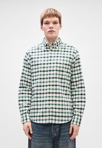 Grønn og hvit rutete knappeskjorte laget av stoff med krage, som har et lite logo på brystet og lange ermer.