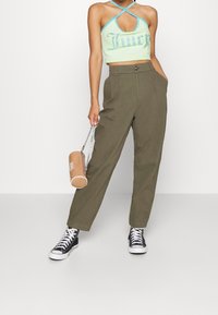 Top corto verde a bretelle con accenti blu, caratterizzato dal testo "Juicy" in strass. Pantaloni a vita alta verde oliva e sneakers nere.