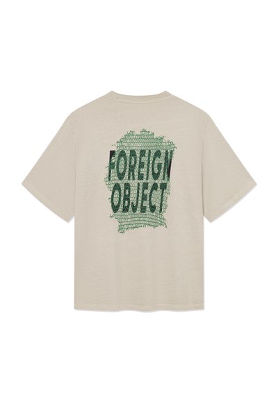 T-shirt beige à manches courtes avec un texte graphique vert "FOREIGN OBJECT" sur un motif cousu dans le dos.