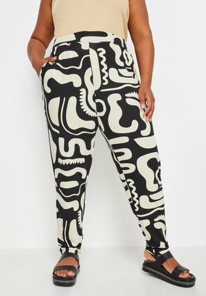 Zwart-witte pantalons met abstracte vormen, een elastische tailleband en zijzakken, gecombineerd met zwarte platform sandalen.